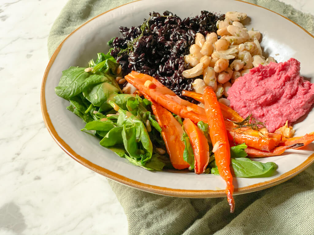 Buddah bowl vegano con hummus de remolacha dobre un plato.